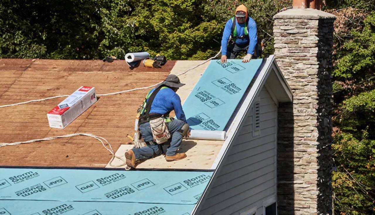 Roofers installing underlayment and seam tape over roof decking