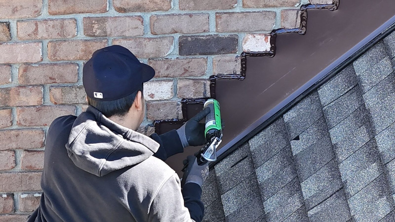 Roofer fitting step flashing where a shingle roof meets a wall