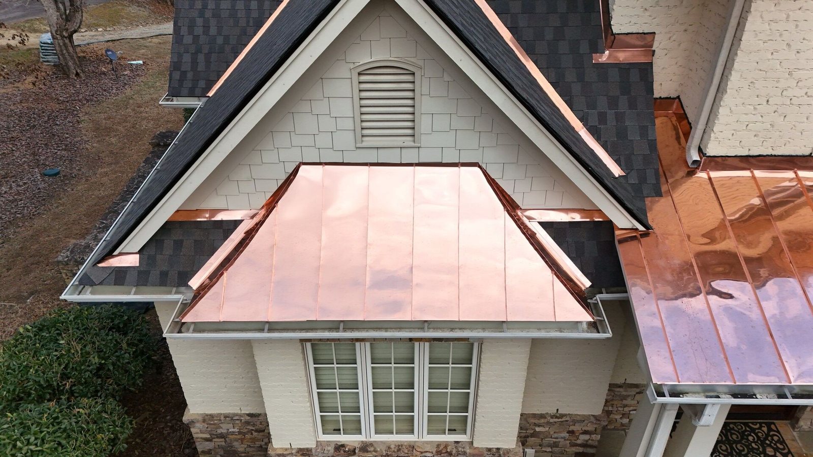 Standing-seam copper metal roof section next to asphalt shingles on the same home