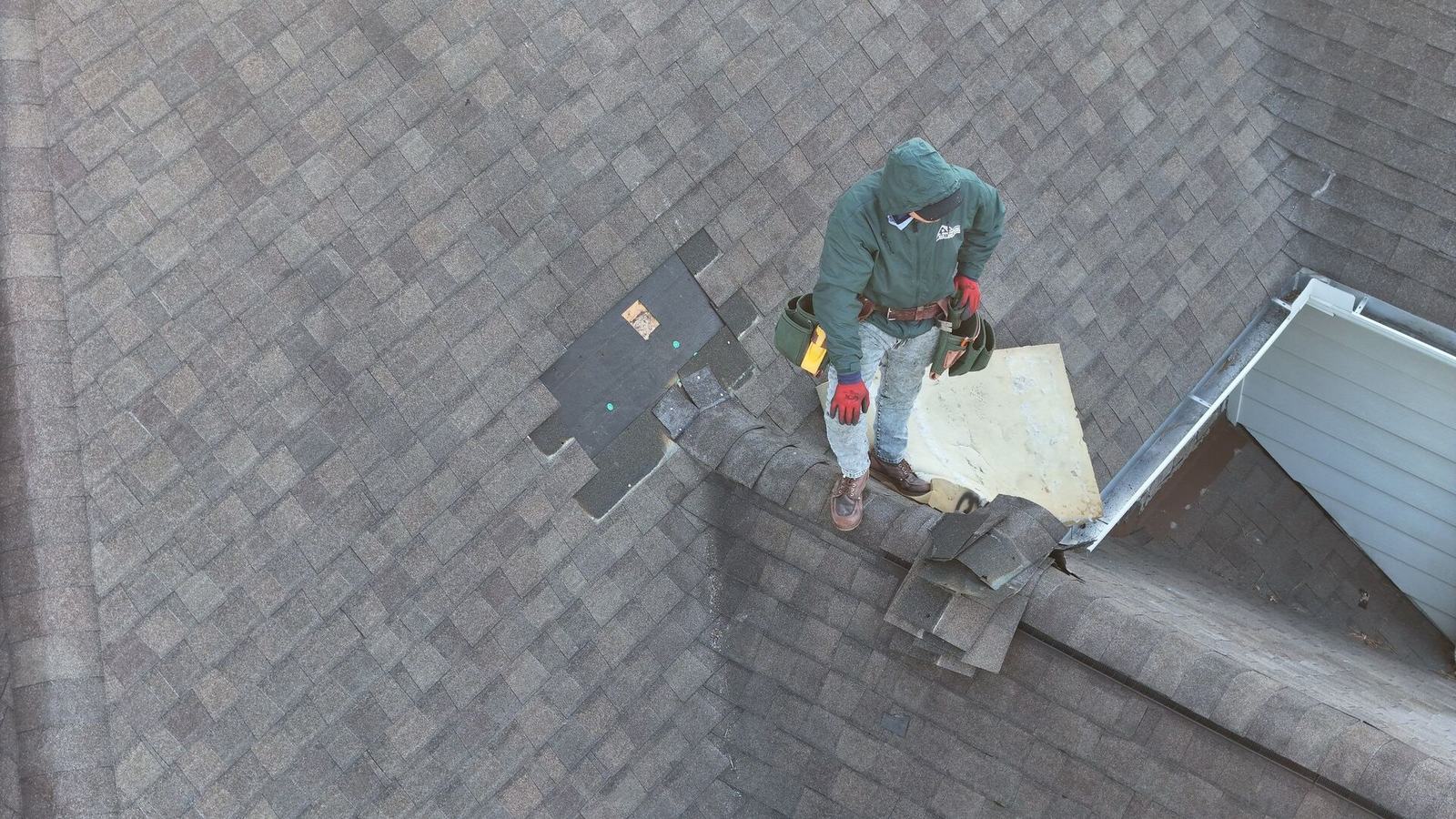 Aerial view of a roofer replacing a patch of shingles on a worn roof