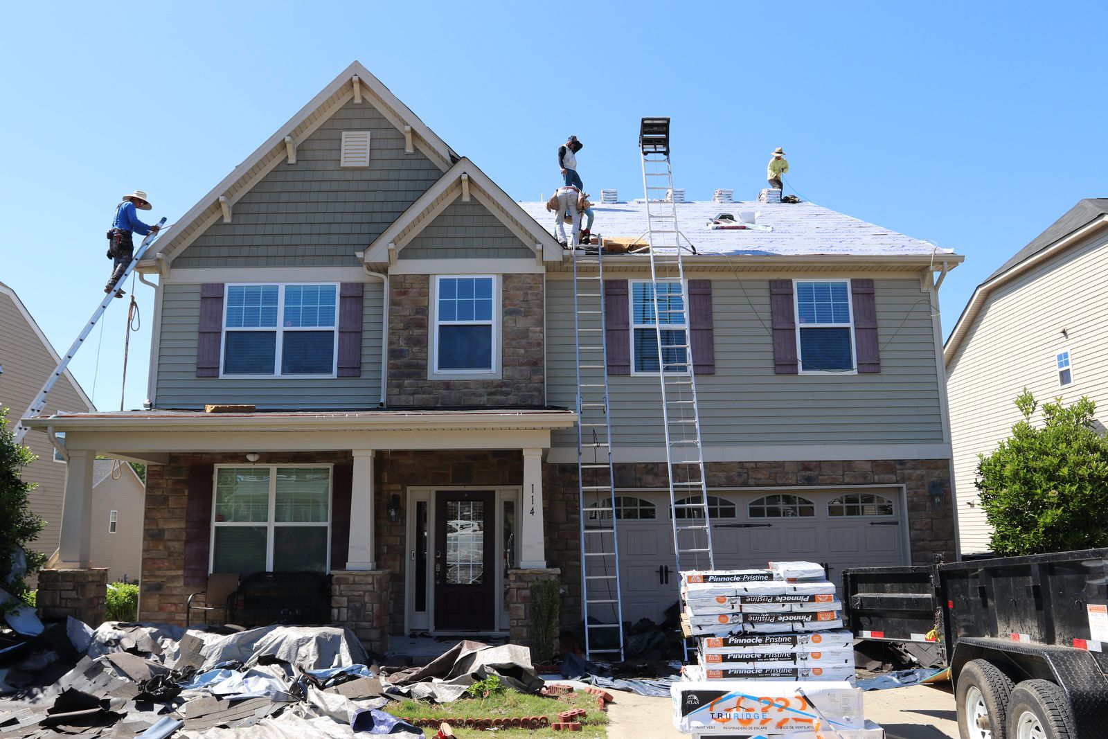 K&D Roofing crew on ladders and roof during a full tear-off, with new shingles staged in the driveway
