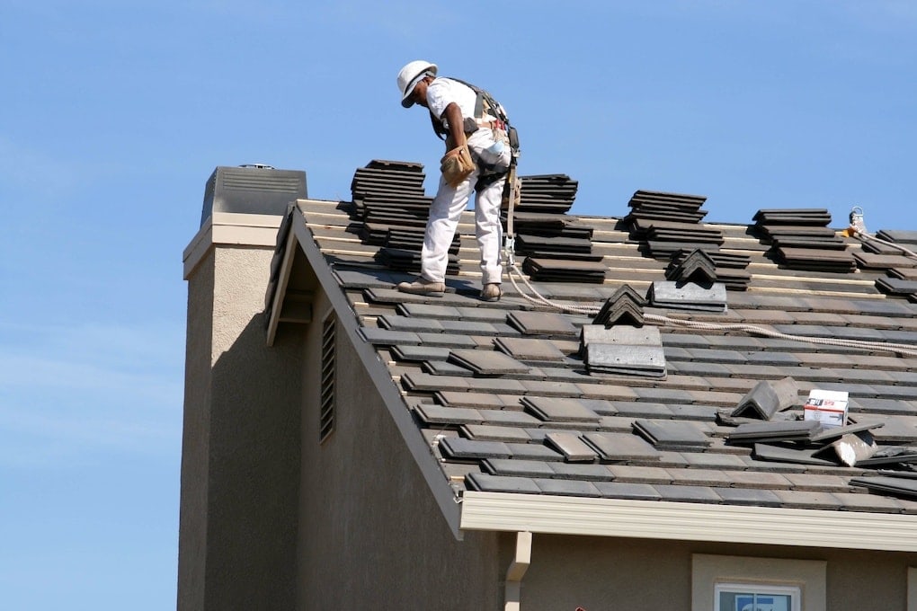 worker installing roof tiles on building with roof warranties; roofing scams to avoid