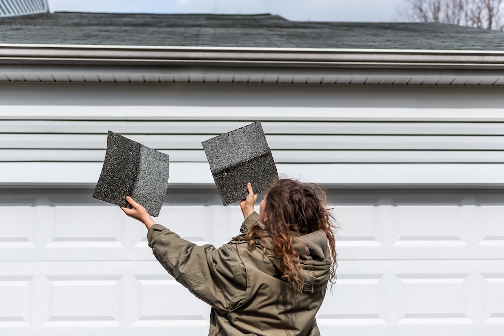 woman inspecting shingles after they were blown off to verify roof warranties 