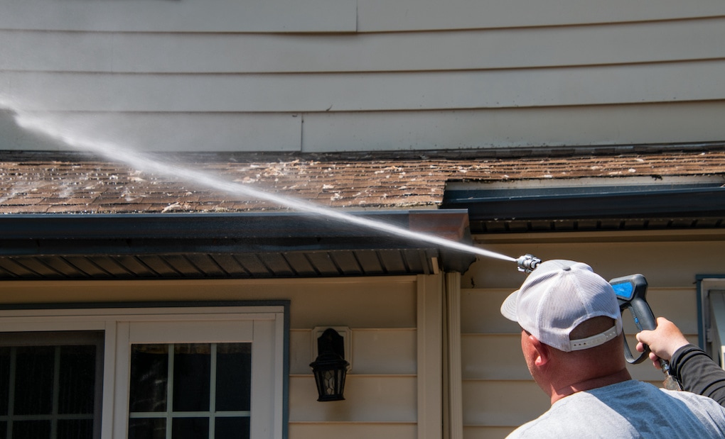 Man with white baseball cap hosing down roof to find a roof leak
