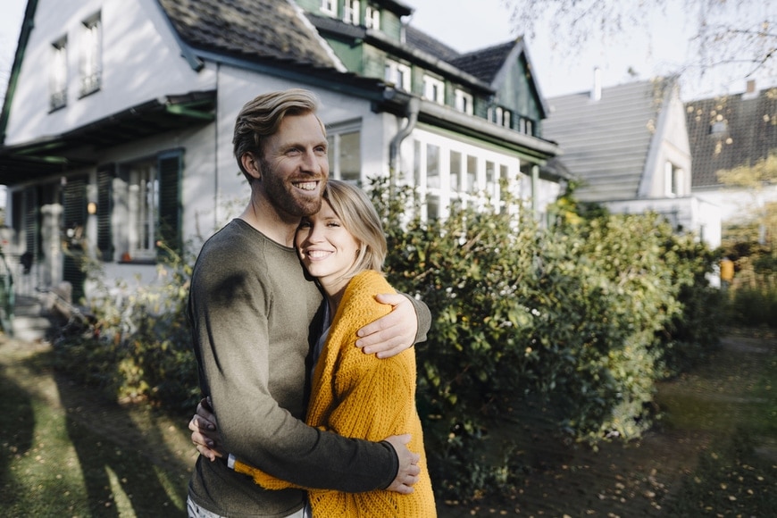 Happy couple embracing in front of their home; roof financing options
