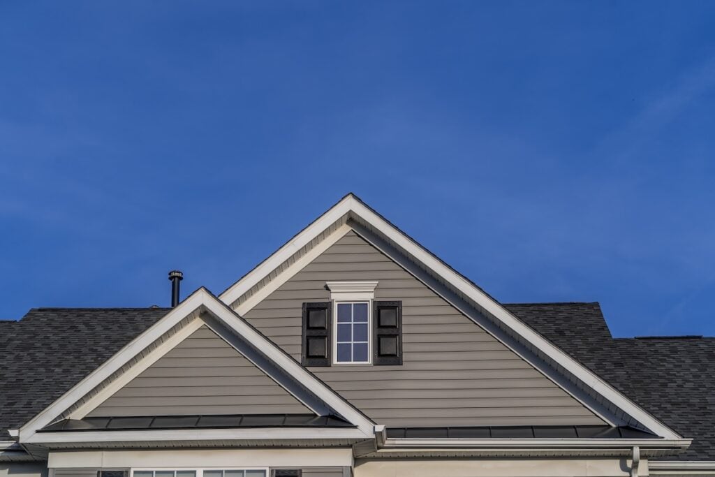Reverse double gable close up on luxury single family residential home. Square single pane gable window. Roof line of traditional home with one gable running one way reverse gables running the other.