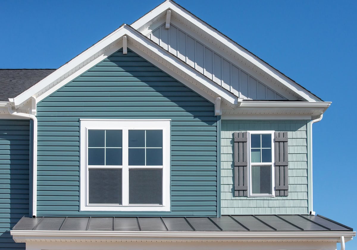 Luxury single family home with natural wood look rough shake finish vinyl Bermuda blue shake and shingle siding, dark metal roof, double pane window with dark shutters, snow trim, venting soffit