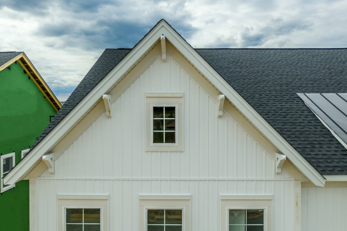 Elegant white gable with attic window, brackets, vertical vinyl lap siding with cloudy sky American real estate vertical vinyl siding