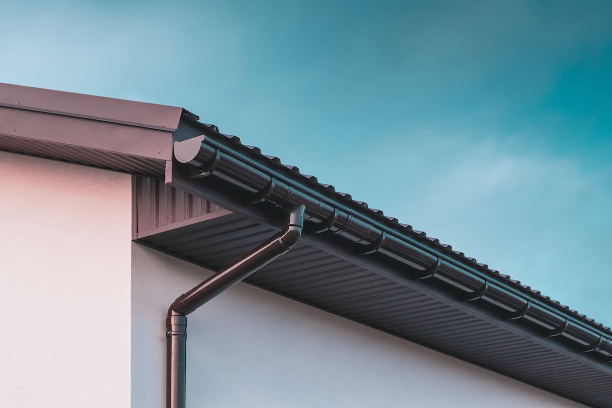 Chocolate-colored plastic gutter on the roof of the building and downpipe on the wall. how to install gutters