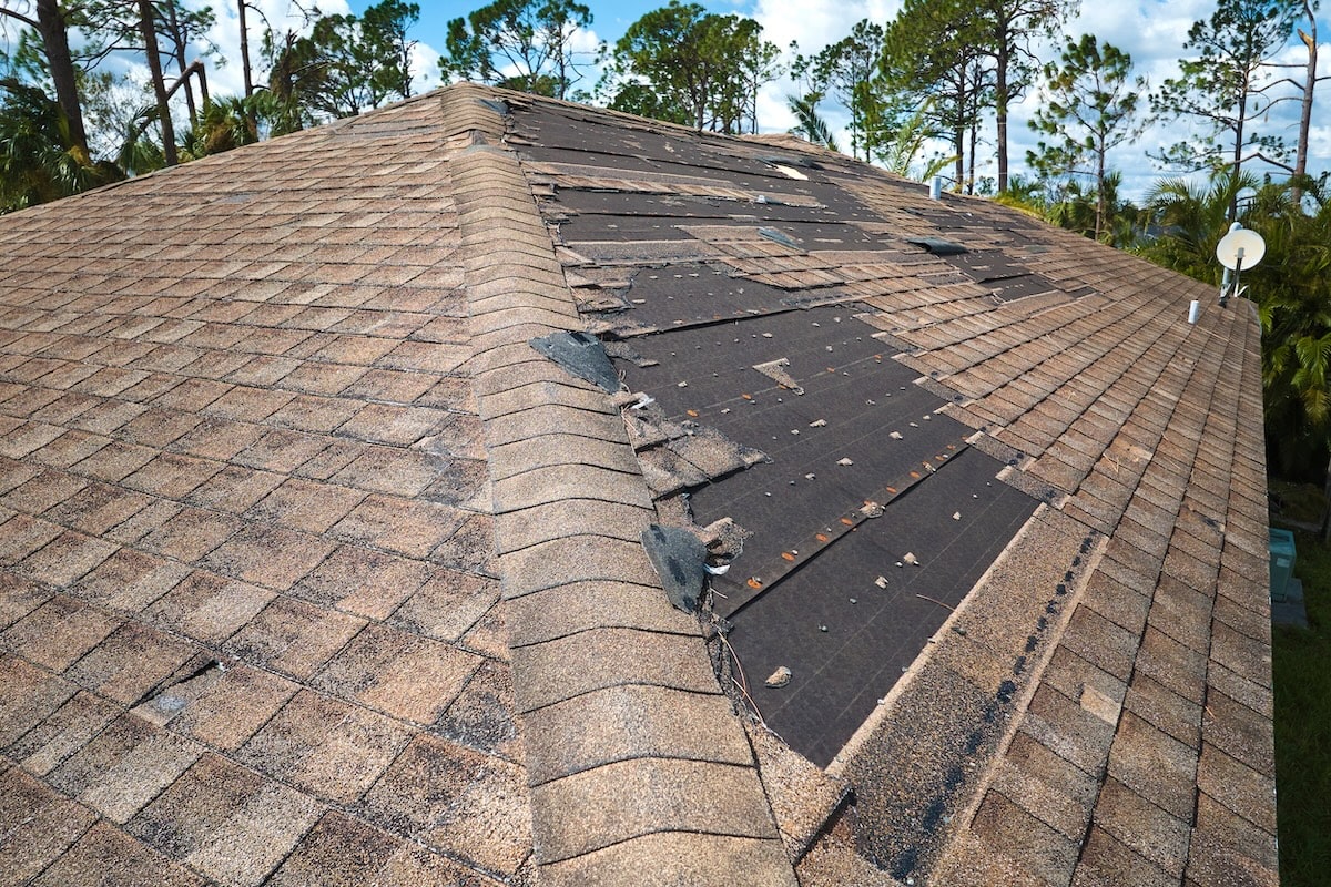 Damaged house roof with missing shingles after hurricane Ian in Florida. Consequences of natural disaster.