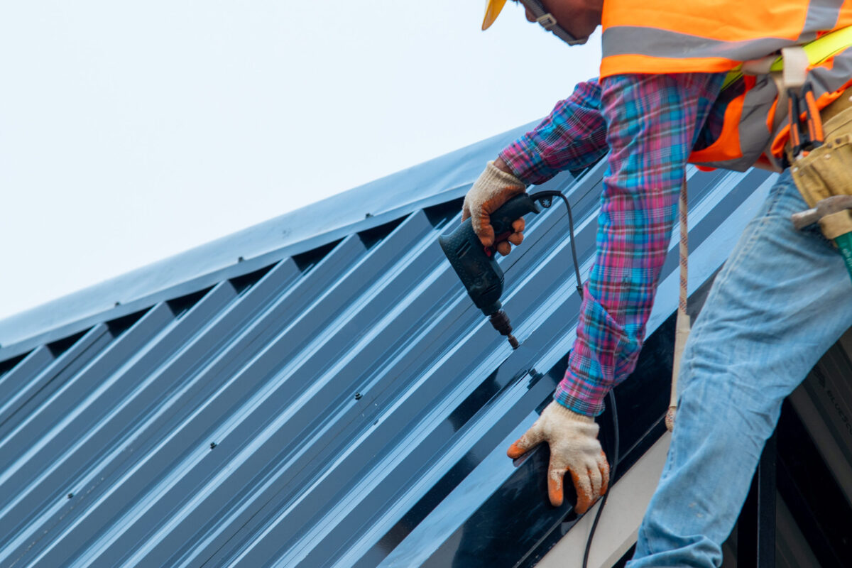 commercial roof replacement Construction worker wearing safety harness belt during working on roof structure of building on construction site,Roofer using air or pneumatic nail gun and installing metal roof tile on top new roof.