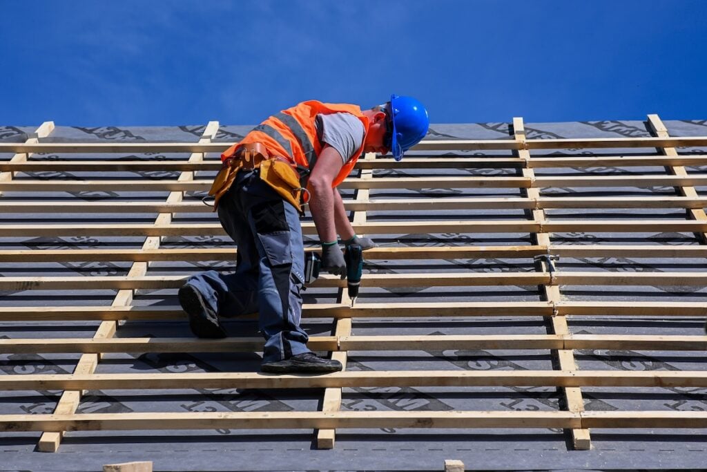 Repair and replacement of the old roof with a new one. Construction worker in protective clothing standing on roof with tools.