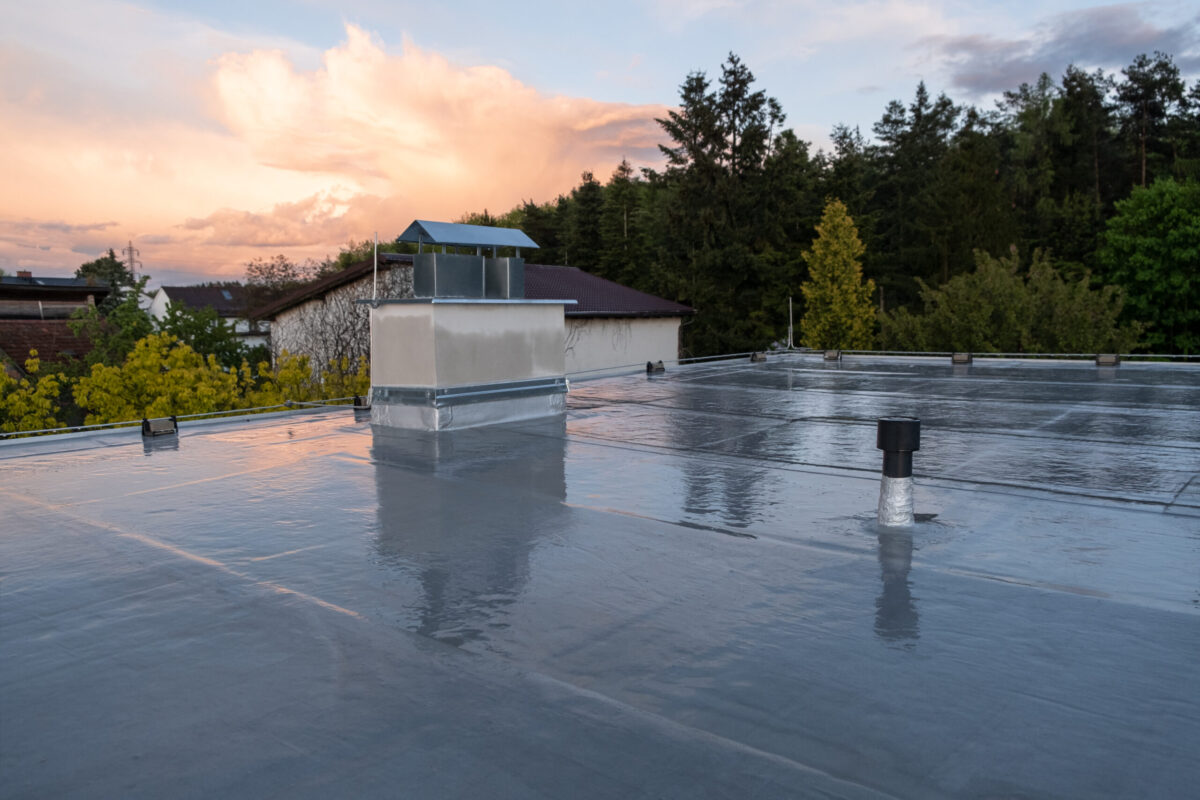 membrane roof Flat roof covered with bitumen membrane and silver lacquer with chimney on a private house. Reflections after rain