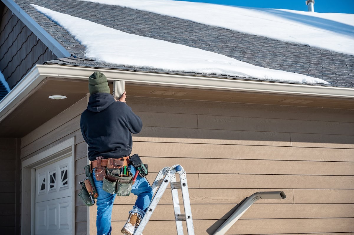 gutter replacement Contractor installing gutters on a residential building in the winter with snow on the roof. High quality photo